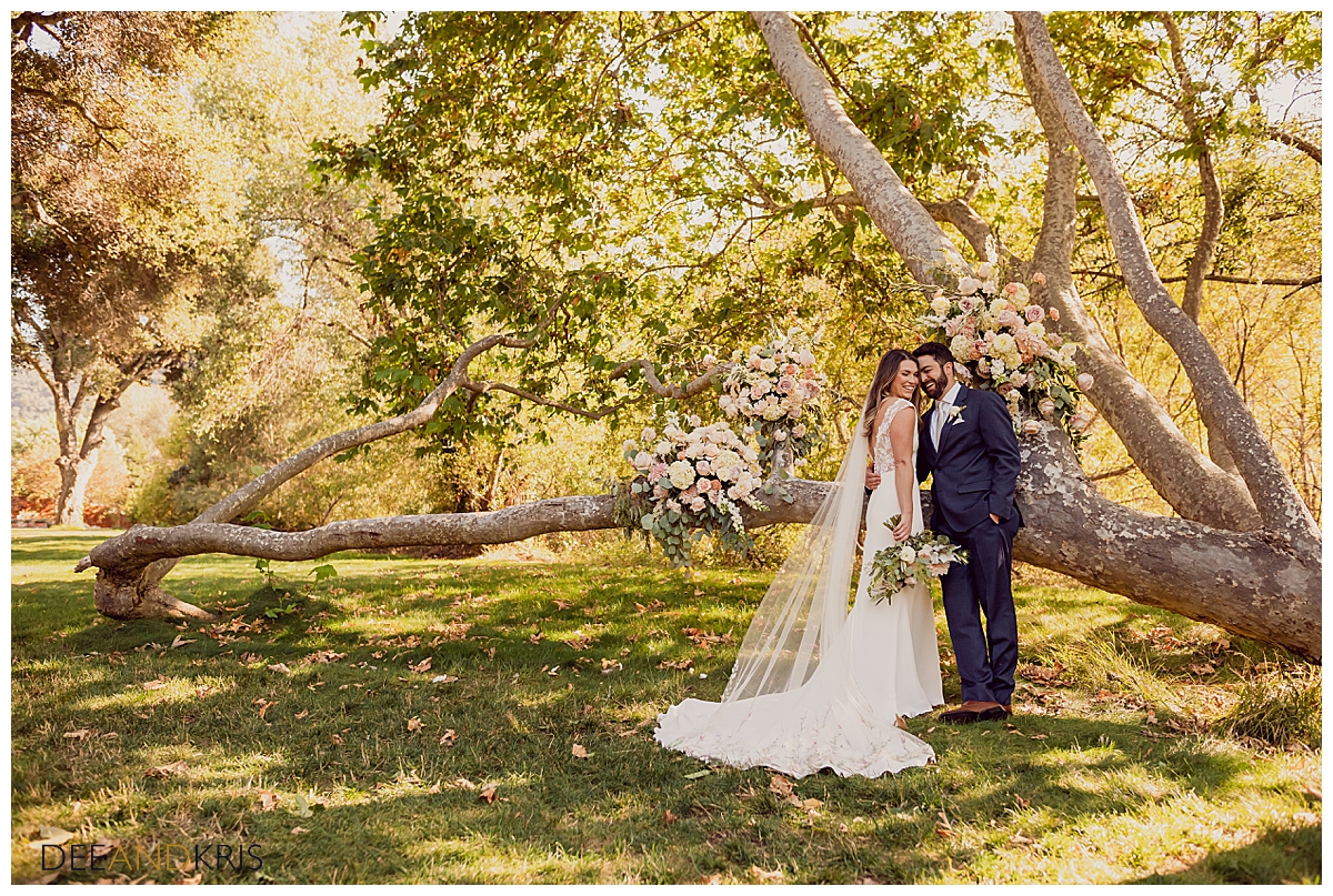 Mairead and Aaron make a lovely couple as they pose forehead to forehead. The new husband and wife lean against a beautiful crooked tree embellished with blush pink and peach colored roses.