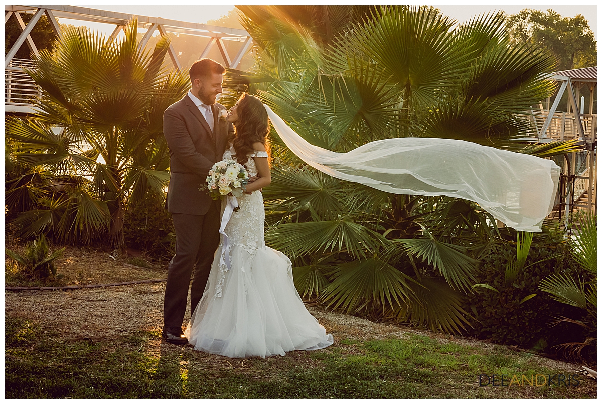 Bride and Groom hold each other in front of the river bridge as the sunsets behind them and her veil flows in the wind.