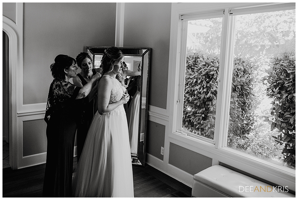 One black and white image of the bride and her mother adjusting the gown in front of a mirror.