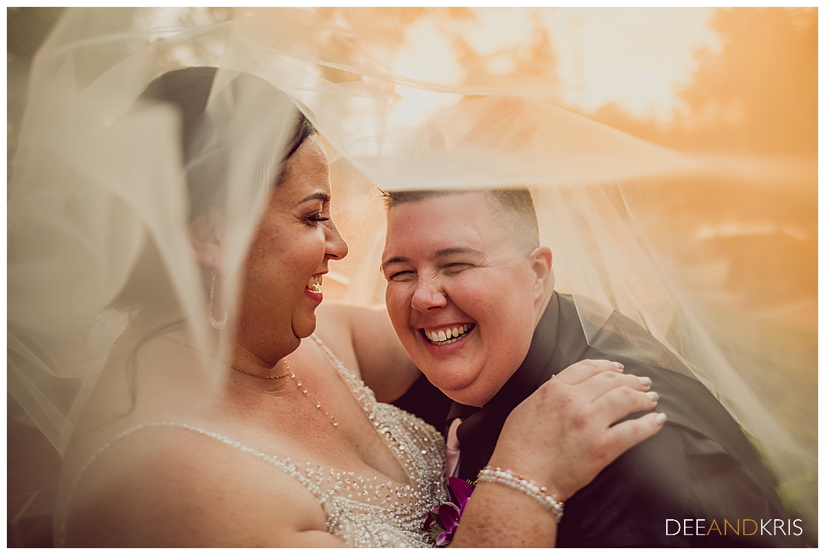 Image of couple enveloped in veil and laughing together.