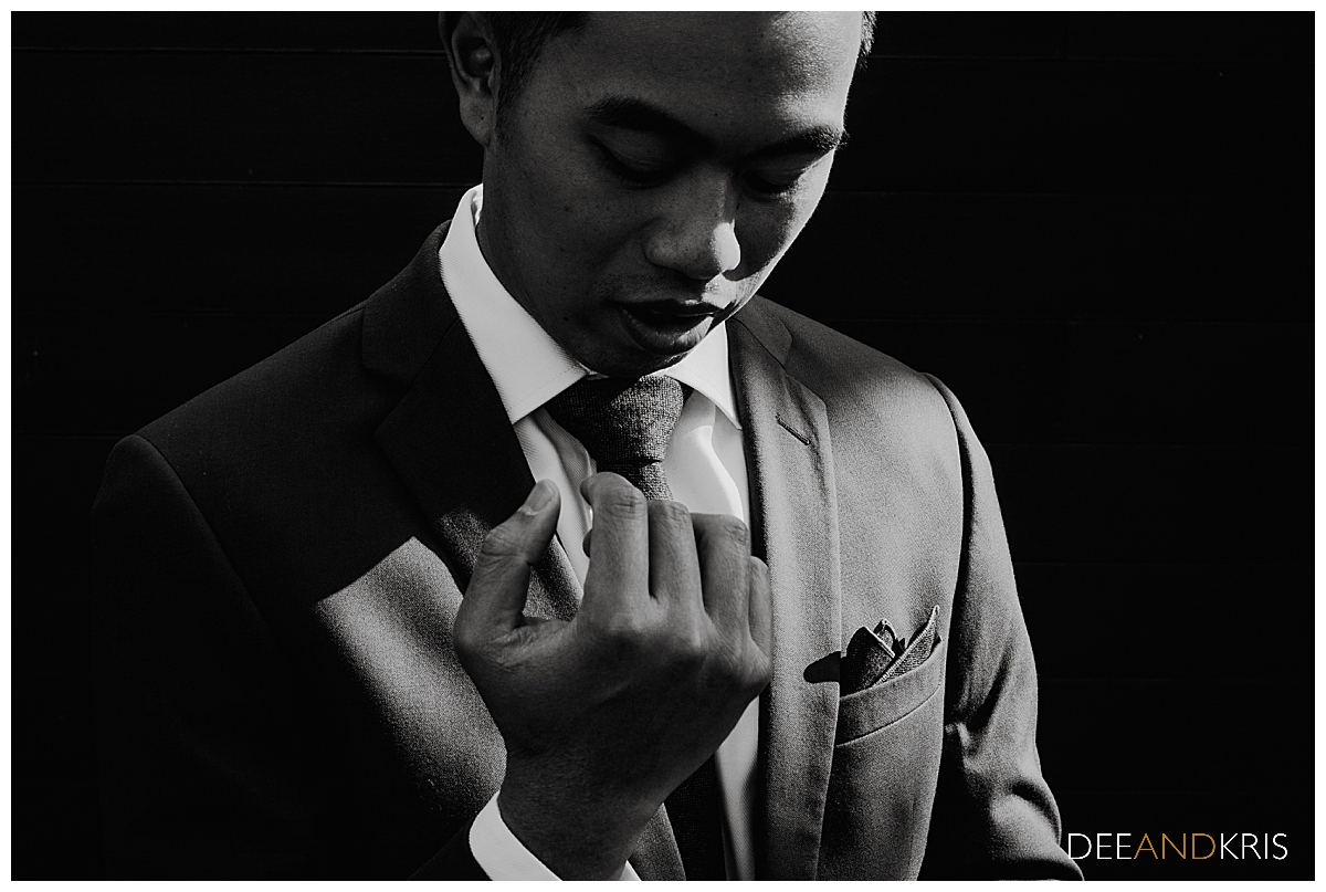 One black and white image of groom in low light adjusting cufflinks.