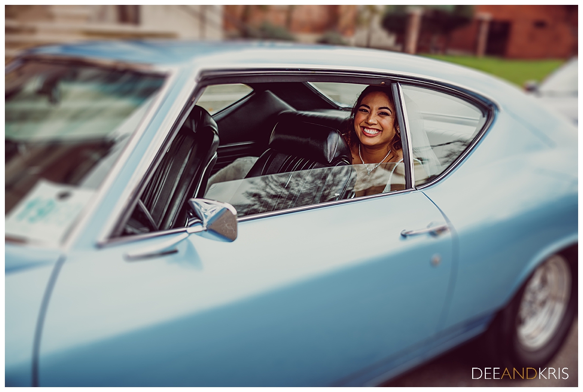 Single image of bride seated in back of blue "69 Chevy Malibu on her way to the Cathedral of the Annunciation.