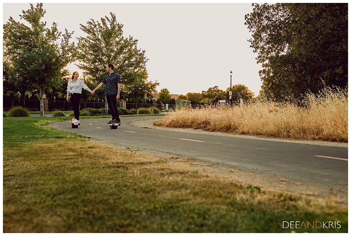 Single image of couple of couple on individual hoverboards holding hands as they glide down a road.