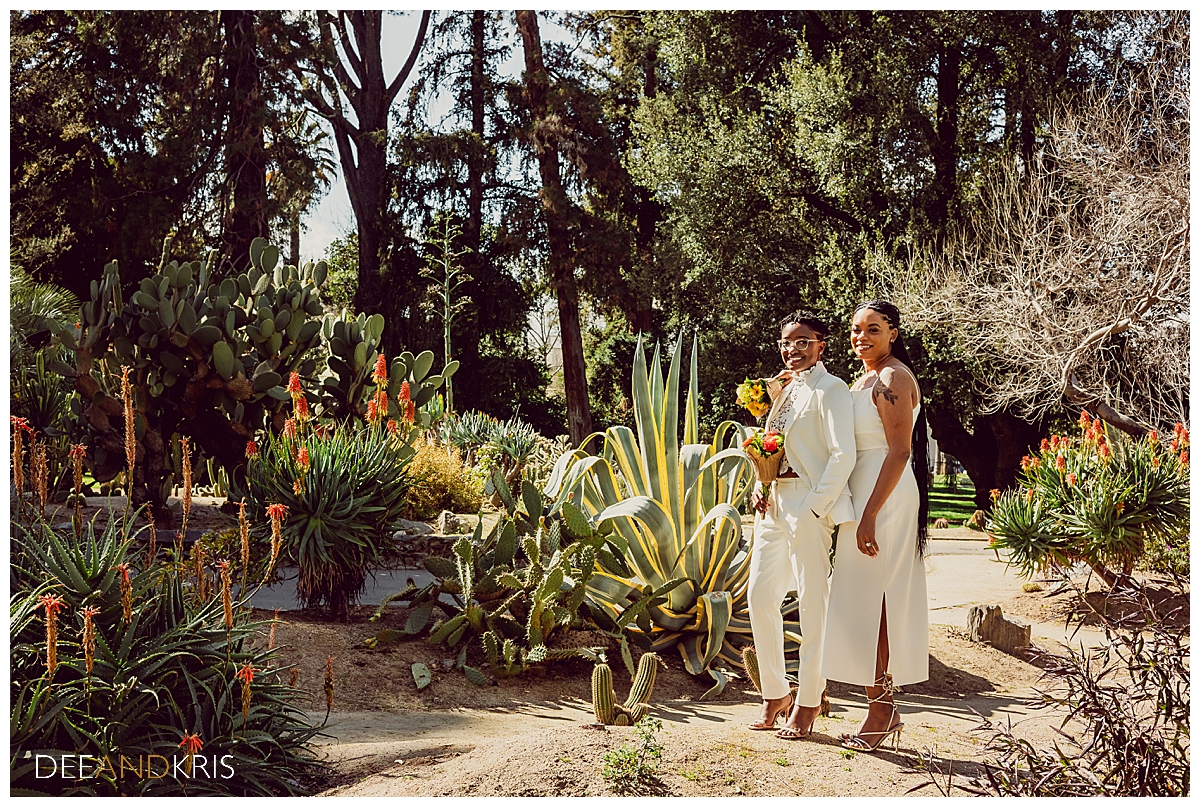 Single image of couple holding bouquets and posing in cactus garden.